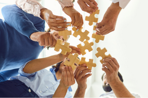 five people's hands in a circle holding puzzle pieces, showing teamworking
